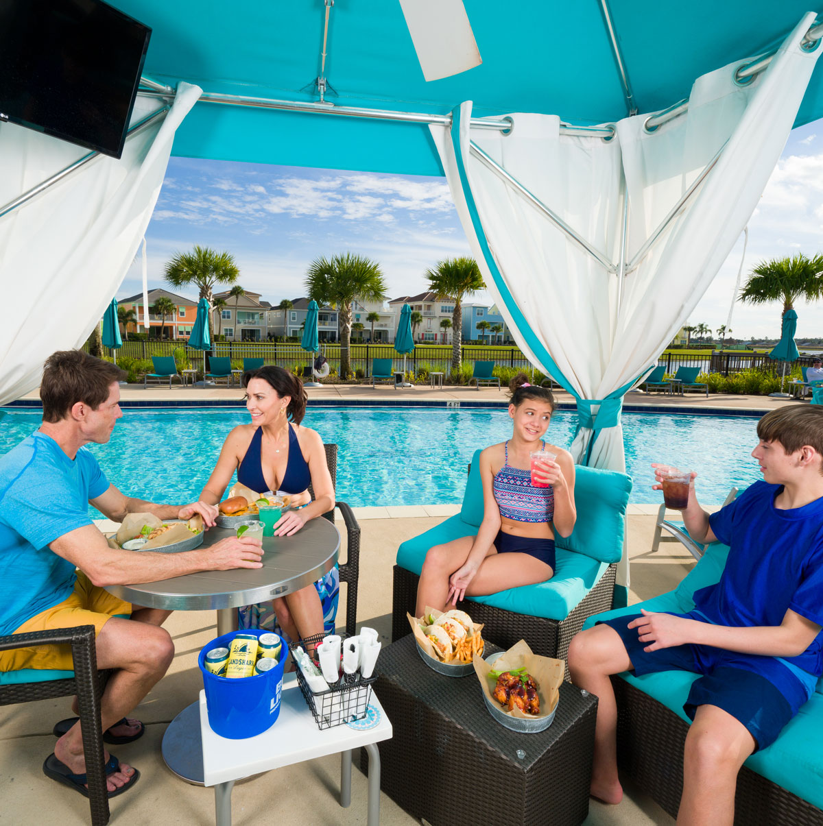 Family of a mom, dad, and two children sharing snacks and drinks under a private cabana at Margaritaville Resort Orlando.