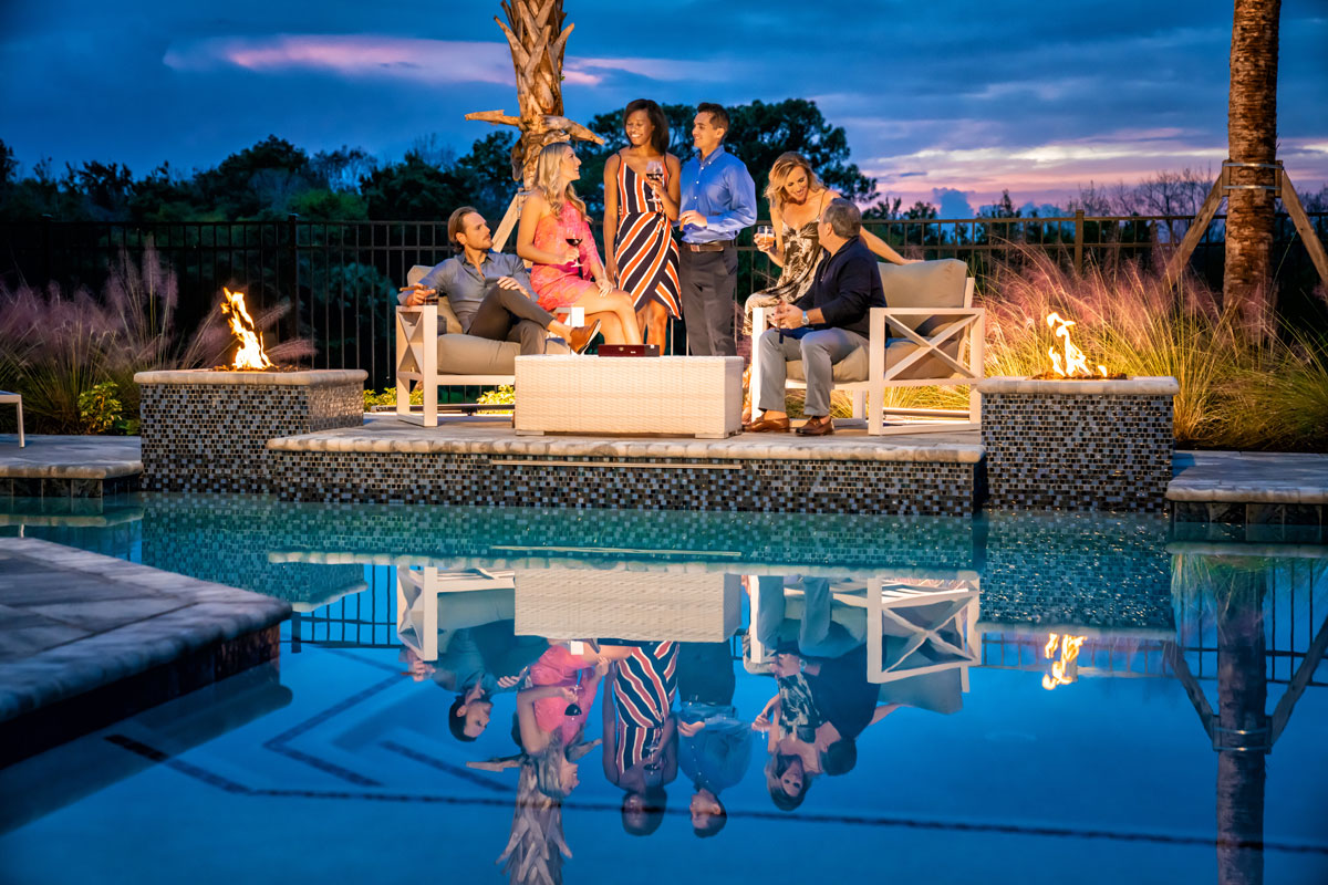 Group of couples sitting and talking together next to a pair of poolside fire pits at Spectrum Resort Orlando at sunset.