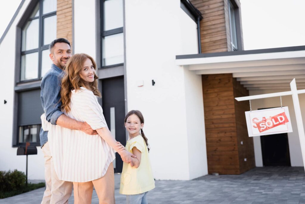 Happy family with young daughter smiling in front of their newly sold home